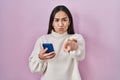 Young south asian woman using smartphone pointing with finger to the camera and to you, confident gesture looking serious Royalty Free Stock Photo