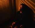 Young Southeast Asian female is exhaustedly leaning against a wall in a dimly-lit room