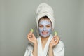 Young spa woman in face mask smiling and holding green cucumber. Female model in blue moisturizing cosmetic mask. Facial treatment