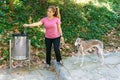 Young Spanish woman with a greyhound dog throwing a bag of her dog\'s feces into a garbage can. Concept of civility and good Royalty Free Stock Photo