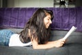 Young Spanish woman smiling and reading a magazine. Home on a sofa. Profil