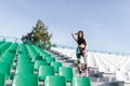 Young sport girl brunette posing at stadium. Fitness girl with a sports figure in leggings and black top standing on the seat in