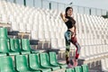 Young sport girl brunette posing at stadium. Fitness girl with a sports figure in leggings and black top standing on the seat in
