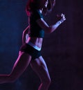 Young sport woman running jogging in gyn in blue and pink neon light on dark wall Royalty Free Stock Photo