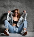 Young sport woman after workout exercise sitting under snow in silver thin down puffer jacket blue jeans Royalty Free Stock Photo