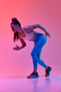 Young sportive girl, professional runner, athlete warming up before run over pink studio background in neon light