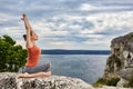 Young sportive woman training yoga asanas on rock above beautiful river.