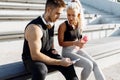 Young sports couple, sitting on the stairs outdoors, listening to music on headphones and using a mobile phone, fitness people Royalty Free Stock Photo