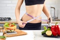 Young sports girl with naked torso measuring her waist with measuring tape in the kitchen. Diet and weigh loss concept Royalty Free Stock Photo