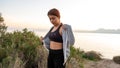 Young sports girl putting on after exercise by the sea over huge cliffs at sunset. She wears tights and sports bra Royalty Free Stock Photo