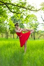 Young sports girl in a red dress practices yoga in a quiet green forest. Meditation and oneness with nature