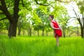 Young sports girl in a red dress practices yoga in a quiet green forest. Meditation and oneness with nature