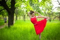 Young sports girl in a red dress practices yoga in a quiet green forest. Meditation and oneness with nature