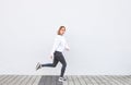 Young sports girl running against the background of a white wall, smiling and looking into the camera