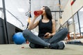 Young sports woman resting on the floor after exercises in gym, drinking water reading smartphone. Fitness, sport, training, Royalty Free Stock Photo