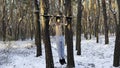 Young sportsman doing static exercises on horizontal bar at forest. Athletic man working out at winter nature. Sportive