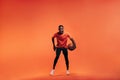 Young sportsman dribbling basket ball in studio against an orange background Royalty Free Stock Photo