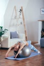 Young sportswoman doing exercises with ball on a mat at home