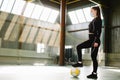 A young sportswoman, dressed in sportswear and with a protective mask, is ready, keeps her foot on a soccer ball. Active