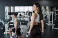 Young sportswoman lifting weights in gym wearing sportswear with her boyfriend on background Royalty Free Stock Photo