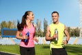 Young sporty couple running with bottles of water at stadium on sunny day
