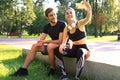 Young sporty couple in sportswear sitting on parapet in urban park and taking selfie after workout on summer sunny day