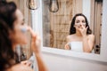 Young sporty dark-haired beautiful woman doing morning evening routine at mirror. She put some mask on face. Beatiful Royalty Free Stock Photo