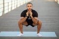 Young sporty man in black fitwear squatting holding dumbbell outdoor Royalty Free Stock Photo