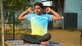 Young sporty man practicing yoga, doing Sukhasana exercise. Black pants and blue shirt, indoor full length, yoga studio Royalty Free Stock Photo