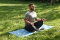 Young sporty man yogi sitting in lotus yoga pose in grass lawn park outdoors