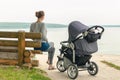 Young sporty mother with stroller sitting on wooden bench near lake or river. Mom walking with baby in pram near pond at early mor Royalty Free Stock Photo