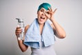 Young sporty woman with blue fashion hair holding bottle of water wearing towel after do sport with happy face smiling doing ok Royalty Free Stock Photo