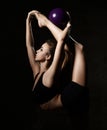 Young sporty woman doing gymnastics stretching fitness exercises workout with purple ball in gym sport club on dark Royalty Free Stock Photo