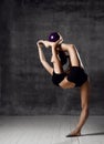 Young sporty woman doing gymnastics stretching fitness exercises workout with purple ball in gym sport club on dark Royalty Free Stock Photo