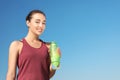 Young sporty woman holding bottle of water against blue sky on sunny day Royalty Free Stock Photo