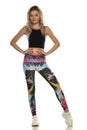 A young sporty woman posing in colorful leggings and a black top on a white background in the studio