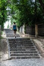 Young sporty woman in sportswear running up steep cobblestone stairs in green alley