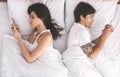 Young spouses using cellphones, ignoring each other in bed Royalty Free Stock Photo