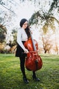 Young standing brunette woman with glasses playing cello at sunset in the park, on a green grass. Vertical Royalty Free Stock Photo