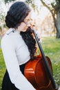 Young standing brunette woman with glasses playing cello at sunset in the park, on a green grass. Vertical Royalty Free Stock Photo