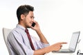 Young business man smiling while talking on the phone and working with laptop computer Royalty Free Stock Photo