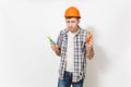 Young strange handsome man in casual clothes and protective orange hardhat holding toy hammer and saw isolated on white Royalty Free Stock Photo