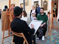 Young street artist draws pencil portrait live of people