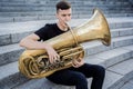 Young street musician playing tuba sitting on granite steps