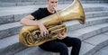 Young street musician playing tuba sitting on granite steps