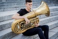 Young street musician playing tuba sitting on granite steps