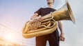 Young street musician playing tuba at the sunset sky background.