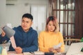 Young stressed asian couple managing finances, reviewing their bank accounts using laptop computer and calculator at modern home. Royalty Free Stock Photo