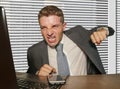 Young stressed and overwhelmed businessman in suit and tie punching laptop computer frustrated and angry working at office desk Royalty Free Stock Photo