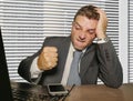 Young stressed and overwhelmed businessman in suit and tie punching mobile phone frustrated and angry working at office laptop Royalty Free Stock Photo